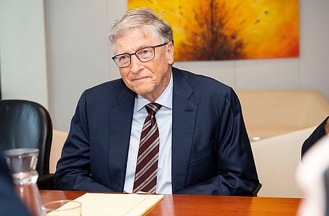 Image of Bill Gates sitting wearing a blue suit at his visit to the European Commission with a yellow blackish painting behind him.
