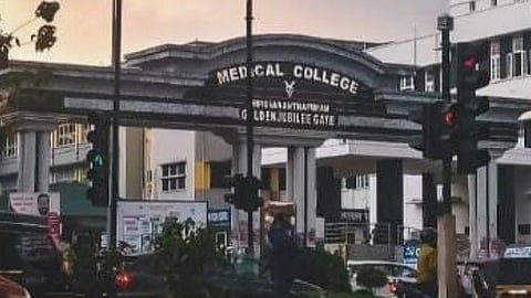 The gate of Medical College with its hoarding with the view of the front road where we can see vehicles and traffic lights.