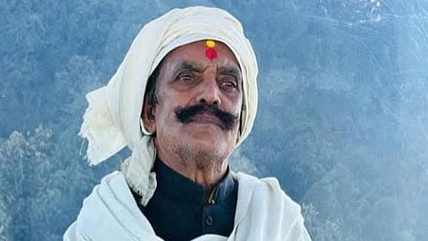 Image of the Jan Suraaj Party worker Dular Chand Yadav who has worn a navy blue Nehru jacket along with a white shawl and a white covering in his head.