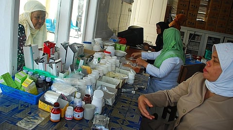 Inside a small Indonesian healthcare centre, staff members are working and there is a patient for the medicine. There are medicine in the table kept for the patients.