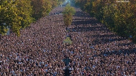 In the image thousand of protesters are shown on the street. The whole road is filled with people and around them are trees