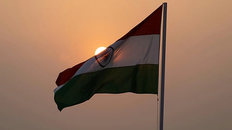 Image of the Indian flag, beautifully hosted with the sun in the background. The sky is in the hues of orange looking beautiful.