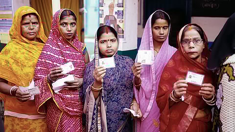 Women voters hold up their EPIC cards while waiting in line to vote in the 2025 Bihar Assembly Elections.