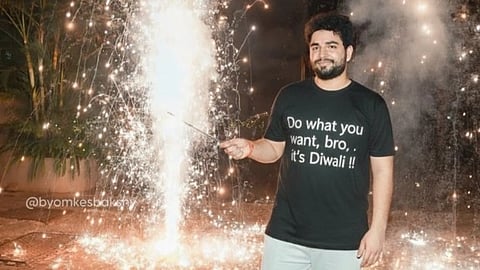 Samay Raina celebrating Diwali, wearing a black tshirt with the text "Do what you want, bro, it's Diwali". There are crackers in the background.