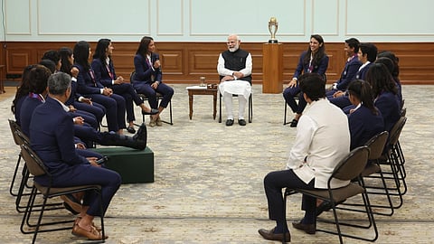 Prime Minister Narendra Modi talking with the Women's cricket team as they won the ICC World Cup for the first time. We can even see the trophy being placed in the background. The mood seems happy.