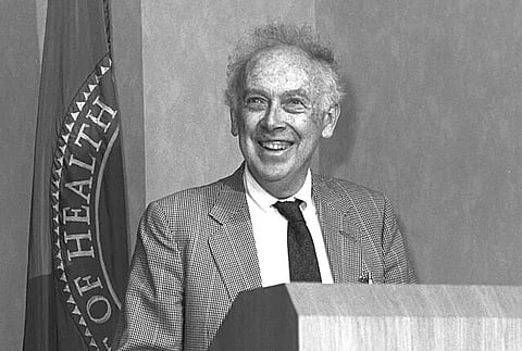 James Watson smiling while standing in front of a podium, black and white.
