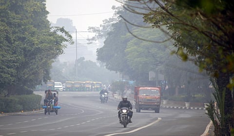 A delhi road covered in pollution, with a truck, bike and rickshaw.
