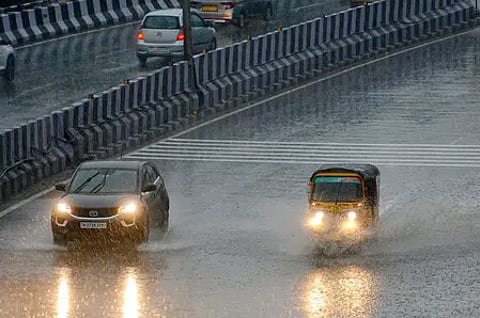 A car and an auto driving through rain and drenched roads with lights on.