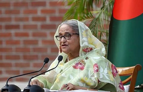 Image of ousted Prime Minister Sheikh Hasina of bangladesh giving a speech with the flag of the country behind her. She is wearing soft green saree with floral design print on it.