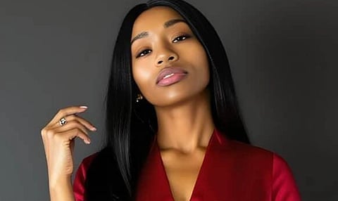 A confident woman in a red satin outfit poses against a dark gray background. She has long, straight black hair and appears poised and serene.