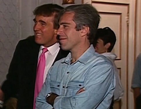 Old Image of Donald trump and Jeffrey Epstein. Trump is wearing a suit with pink tie and Epstein is wearing his blue shirt, Both are looking at someone and smiling.