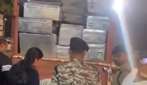 In the image a truck full of tin boxes is shown and a police officer and other people are looking at them