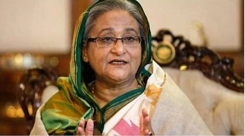 In the image former Prime minister Skeikh Haseena is shown talking to someone. She is wearing a saree and sitting in a sofa