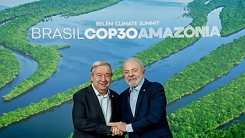 Brazil’s President Lula da Silva (right) standing with UN Secretary General Antonio Guterres in front of a COP30 board with a view of the amazon river and forested land in between.