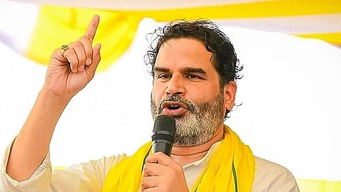 Prashant Kishor speaks passionately into a microphone, raising one finger. He wears a white shirt and a yellow shawl, with a determined expression.