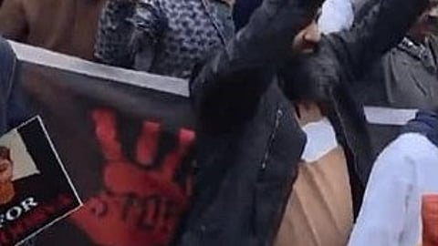 Protesters gather outside St. Columba's School holding signs demanding justice, featuring images and red handprints. The mood is intense and determined.