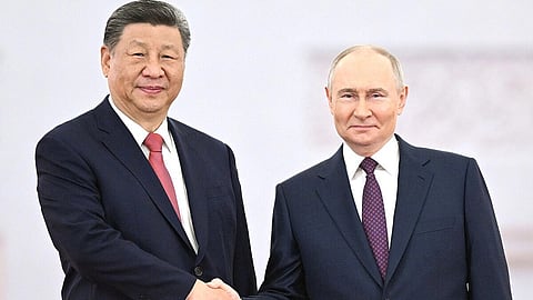 In the image Xi Jingping and Vladimir Putin are shown shaking hands both are wearing formal suits with Xi jingping wearing red tie and Putin wearing purple.