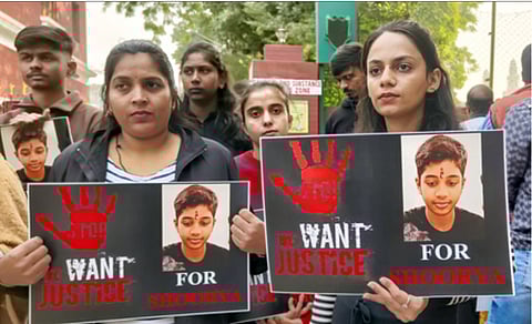 A group of concerned individuals holds signs demanding justice for Shoorya, featuring a red handprint and the phrase "We Want Justice." The mood is serious and determined.