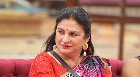 In the image Kunickaa Sadanand is shown wearing a saree looking on her right smiling, Her blouse is red and her saree is printed with patterns