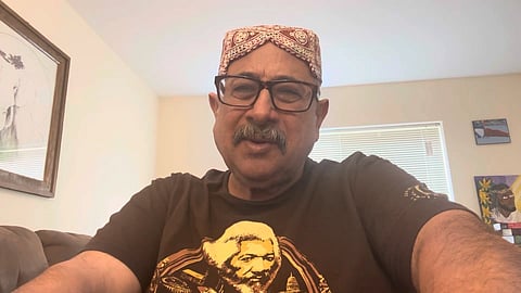 A screenshot of a YouTube video uploaded by Ahmar Mustikhan. He is in a living room with a window behind him, wearing a Bugti topi.