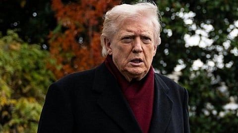 Elderly man in black coat and red scarf stands outside on a cloudy day with autumn foliage, conveying a serious expression.