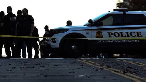 A police SUV and officers stand behind yellow tape on a street, creating a sense of urgency and seriousness. The scene is dimly lit, suggesting evening.