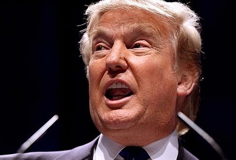 Image of US president Doanld trump with light hair speaking at a podium with microphones. Their expression seems animated, possibly in a public speaking context.