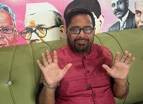 Image of Bihar journalist Kanahiya Bhelari in a red vest and glasses. He is sitting on a green couch, smiling with hands raised.