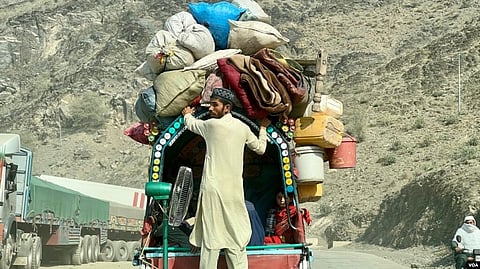 An Afghan refugee returning to Afghanistan in 2023. He stands in front of a wagon, with his family inside, luggage on top, and a fan behind him.