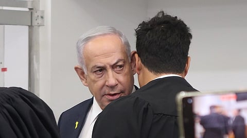 Benjamin Netanyahu in court during his corruption trial, prior to his third testimony day, seems to be talking with his attorney, Amit Hadad, with his back to the camera.