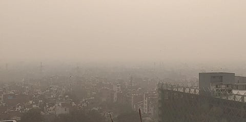 A hazy cityscape under heavy smog, obscuring distant buildings. The air appears thick, evoking a sense of pollution and environmental concern.