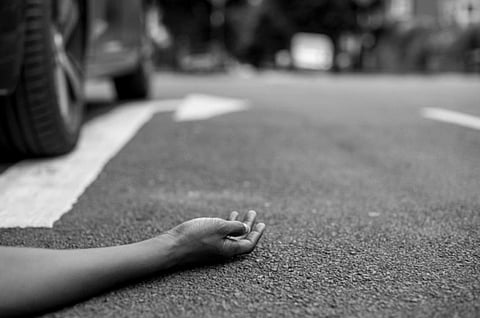 A hand lies motionless on a street beside a car tire. The scene suggests an accident, conveying a dramatic and tense atmosphere.