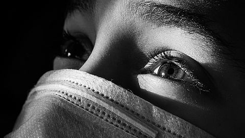 Close-up of a person's face in black and white, wearing a mask. Light highlights their eye, conveying a sense of introspection and hope.