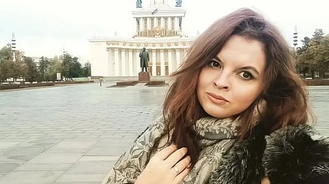 Picture of journalist Nika Novak with long brown hair taking a selfie in front of a large classical building with columns and ornate details. A statue stands in the plaza.