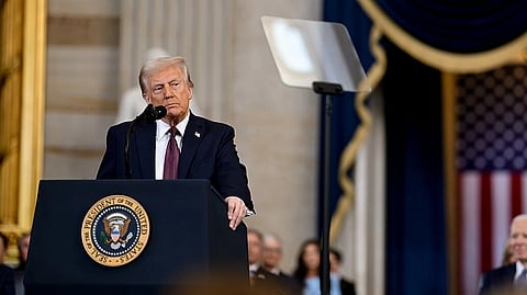 Speech by a Donald Trump at a podium with the presidential seal, ornate backdrop, and audience. American flag creates a solemn tone.