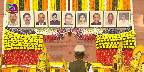 The image depicts 9 martyrs who fell during 2001 Parliament terrorist attacks. It is the main Parliament House building, and flowers are laid upon the martyrs images.