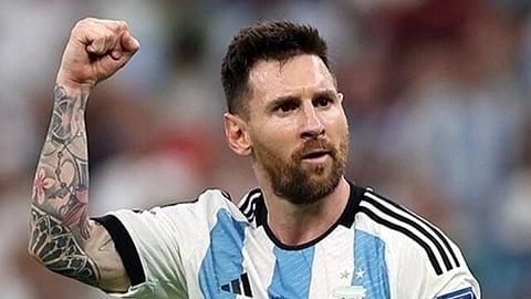 Soccer player in a white and blue striped jersey with number 10, raises a fist in celebration. Lionel Messi has a determined expression and a tattooed arm.