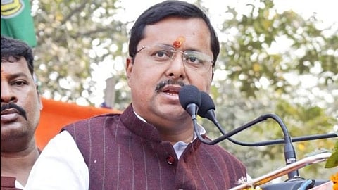 Bihar Minister Nitin Nabin in traditional Indian attire speaks at an outdoor podium adorned with orange marigold garlands.