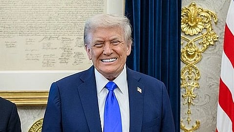 In the image Donald Trump is shown wearing a blue suit with light blue tie behind him is a Half America flag