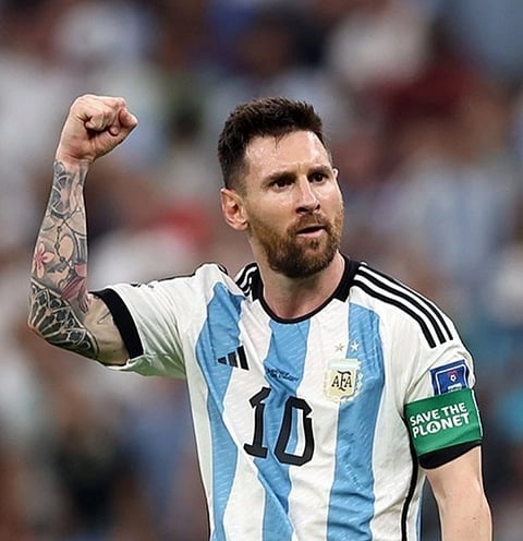 Lionel Messi in Argentina football jersey, with his right arm raised as indicating to a victory. He's wearing the captain's armband, with Save The Planet written on it.