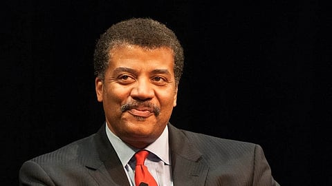 Neil De Grasse portrait's depicts him wearing a suit, smiling and the background is black.