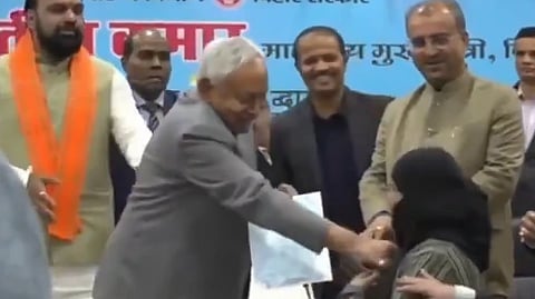 Image of Bihar CM Nitish Kumar pulling down a woman's hijab in a government event. Behind him 4 people are standing. one on the extreme left is deputy minister Samrat Chaudhary.