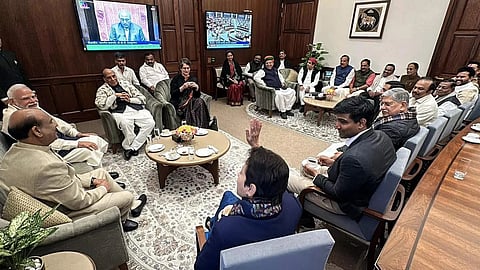 The image depicts several leaders of India in a tea gathering hosted by Lok Sabha speaker Om Birla. The image shows PM Modi, Om Birla, Rajnath Singh, Priyanka Gandhi and various other leaders. In the centre, there is a small circular table, and the MPs are sitting around in chairs and sofas.