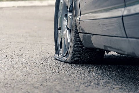 Close-up of a car with a flat tire on an asphalt road. The deflated tire sidewall is touching the ground, conveying a sense of inconvenience or urgency.