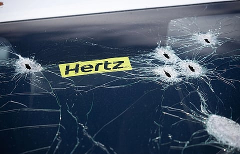 Image of Bucha after Russian invasion of Ukraine. it depicts Cracked car windshield with six bullet holes near a yellow Hertz sticker. The image conveys damage, contrast, and tension.