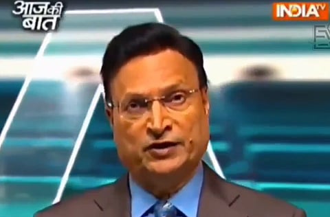 Image of journalist Rajat Sharma on his show Aaj ki Baat. He is wearing a grey suit with blue shirt and a blue tie. On the top right corner India Tv is written and on the top left Aaj ki Baat is written in Hindi font.