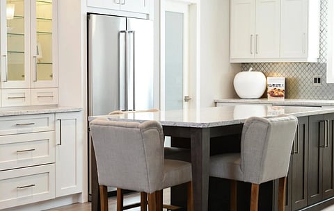 Modern kitchen with a sleek design featuring a marble countertop island, gray upholstered chairs, stainless steel fridge, and white cabinetry. Luxurious and inviting atmosphere.