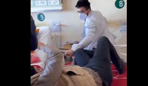 A healthcare worker in a mask beating a patient in a hospital bed. Bed numbers 8 and 9 are visible.