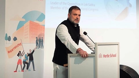 Leader of Opposition and congress Leader at podium in at the Hertie School in Berlin, Germany. A banner and presentation screen in the background convey an academic event.