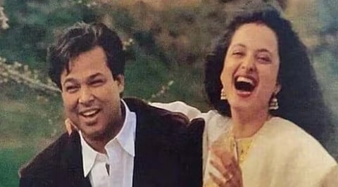Image of Rekha and her husband Mukesh Aggarwal. the couple can be seen smiling . The man wears a dark coat and white shirt, the woman a light dress. The background is lush greenery.